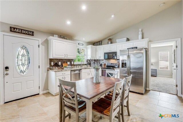 kitchen with appliances with stainless steel finishes, light stone counters, white cabinets, decorative backsplash, and vaulted ceiling