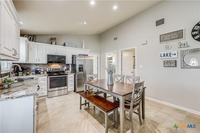 kitchen featuring appliances with stainless steel finishes, white cabinetry, sink, backsplash, and light stone countertops