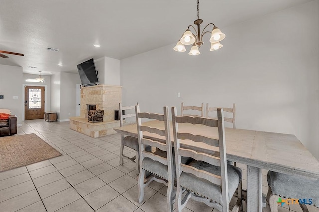 tiled dining room with ceiling fan with notable chandelier and a fireplace