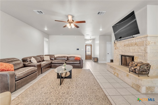 living room with a stone fireplace, ceiling fan, and light tile patterned flooring