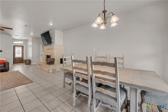 tiled dining space with ceiling fan with notable chandelier and a fireplace