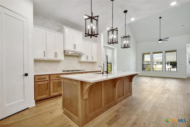 kitchen featuring light wood finished floors, open floor plan, a kitchen island with sink, light countertops, and under cabinet range hood