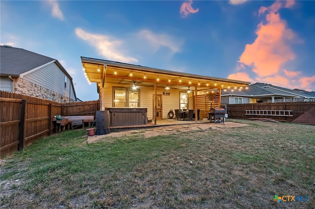 back of house featuring a fenced backyard, a hot tub, a patio area, and a lawn