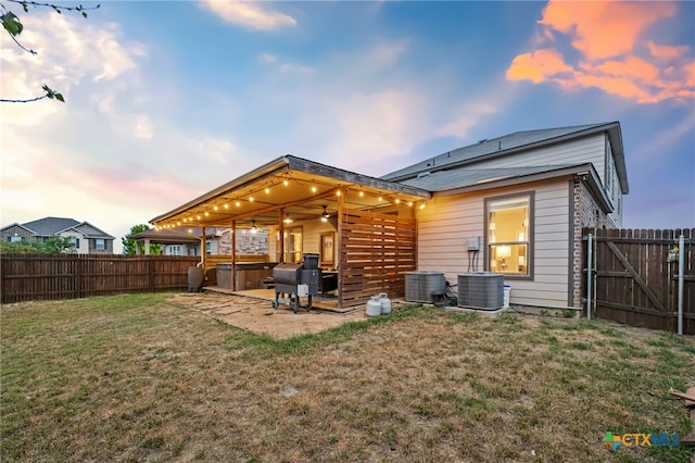 back of house at dusk with a lawn, a hot tub, a fenced backyard, and ceiling fan