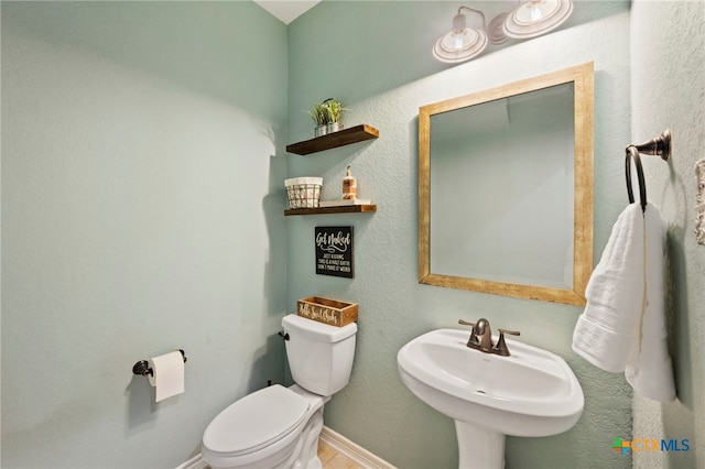 half bath featuring toilet, a sink, and baseboards
