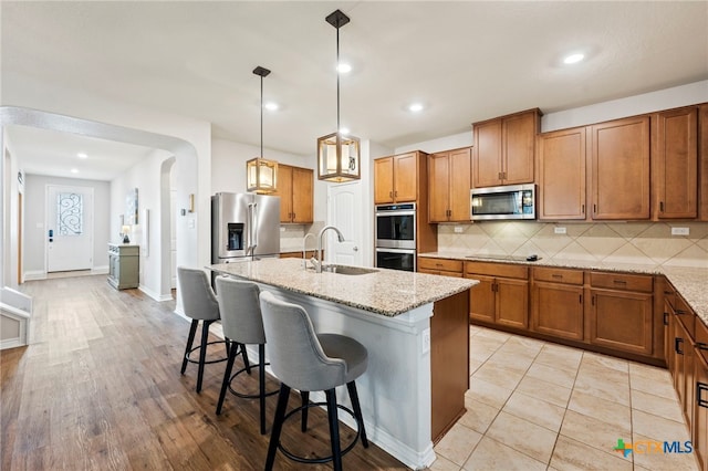 kitchen featuring brown cabinetry, decorative backsplash, stainless steel appliances, and a sink