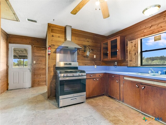 kitchen featuring wood walls, stainless steel gas range oven, a textured ceiling, and extractor fan