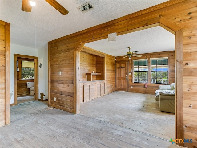 unfurnished living room featuring a textured ceiling, wooden walls, and ceiling fan