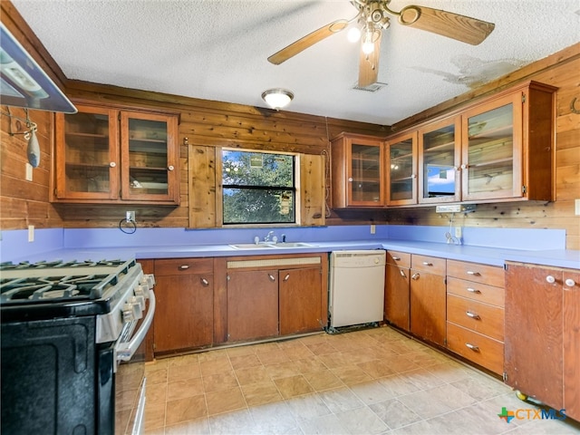 kitchen with wood walls, gas range, a textured ceiling, and white dishwasher