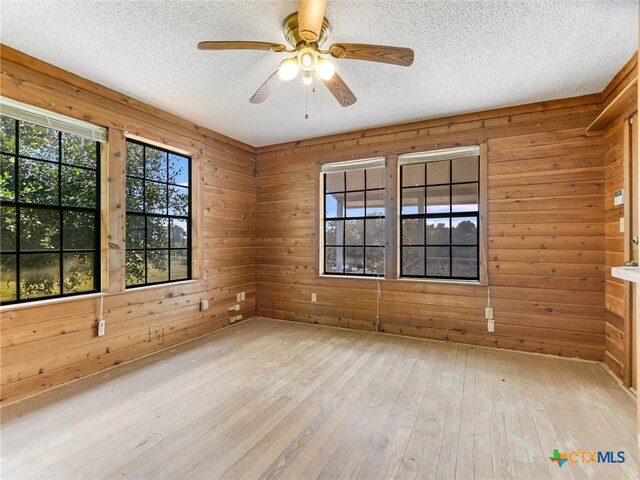 empty room with a textured ceiling, light hardwood / wood-style floors, wood walls, and ceiling fan