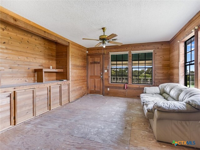 unfurnished living room with a textured ceiling, wood walls, a healthy amount of sunlight, and ceiling fan