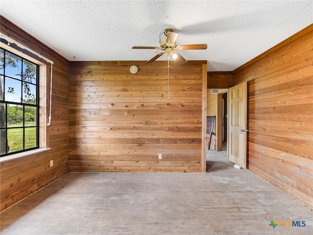 empty room with wood walls, ceiling fan, and a healthy amount of sunlight