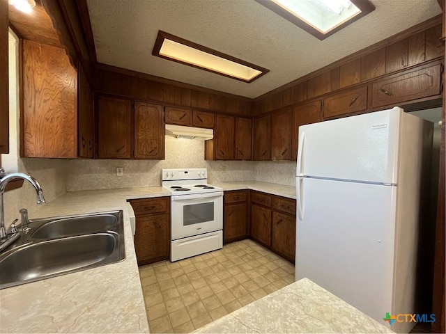 kitchen with under cabinet range hood, white appliances, light countertops, and a sink