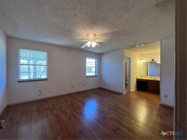 unfurnished bedroom featuring connected bathroom, baseboards, a textured ceiling, and wood finished floors