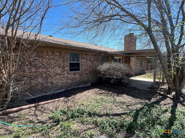 back of house with brick siding and a chimney