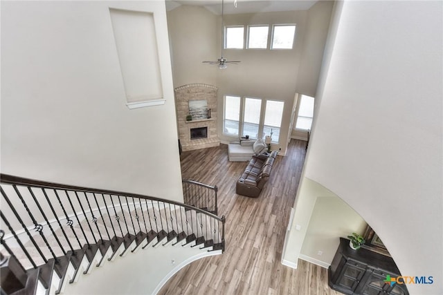 stairs featuring ceiling fan, a wealth of natural light, wood-type flooring, and a stone fireplace