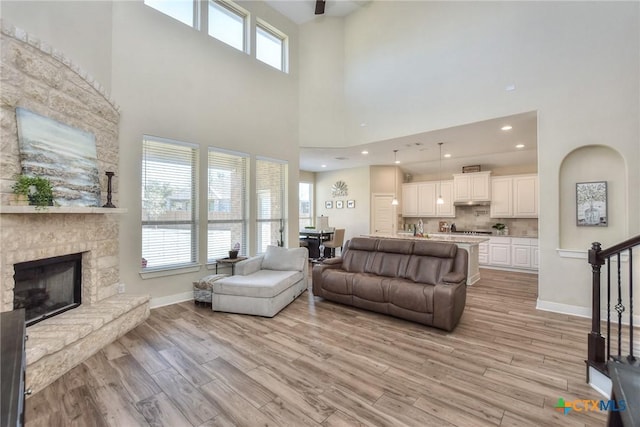 living room with a stone fireplace, a towering ceiling, and light wood-type flooring