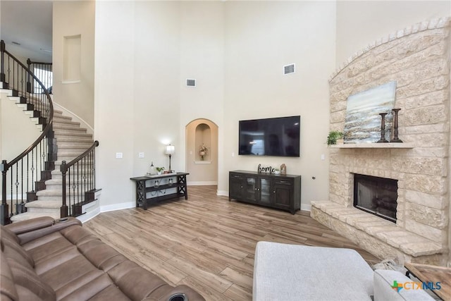 living room with light wood-type flooring, a towering ceiling, and a stone fireplace