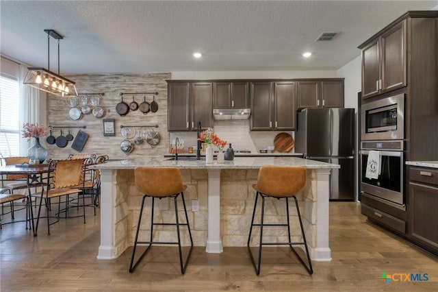 1531 Esser Xing, Canyon Lake, TX 78132 - kitchen with appliances with stainless steel finishes, under cabinet range hood, dark brown cabinets, a breakfast bar area, and a textured ceiling