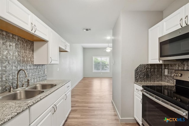 kitchen with white cabinets, appliances with stainless steel finishes, backsplash, and light hardwood / wood-style flooring