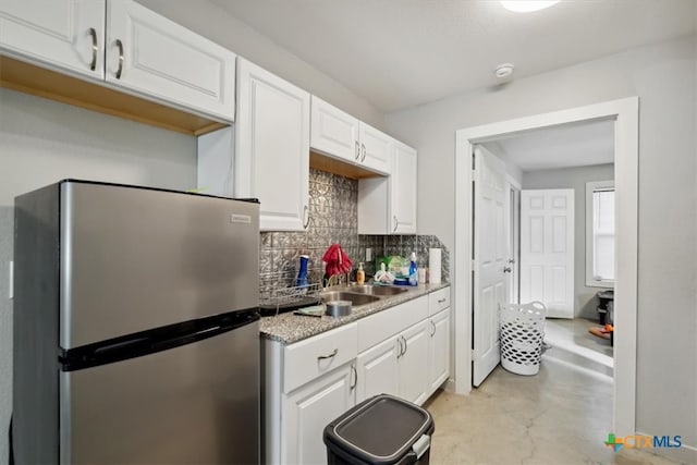 kitchen featuring light stone counters, stainless steel fridge, white cabinetry, backsplash, and sink