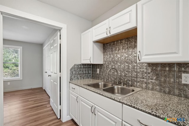 kitchen with light wood-type flooring, sink, light stone countertops, and white cabinets