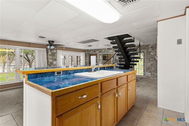 kitchen featuring ceiling fan, light colored carpet, sink, and a center island with sink