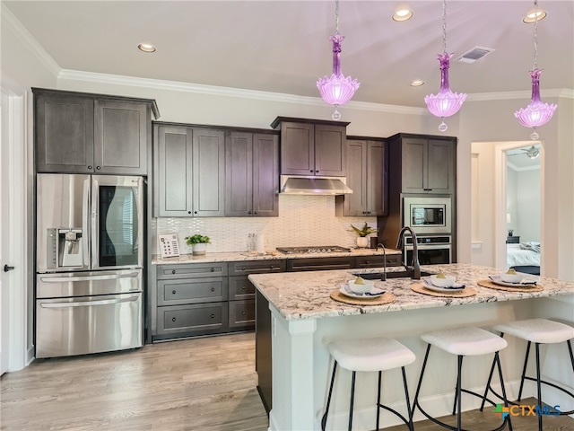 kitchen with dark brown cabinetry, a breakfast bar area, appliances with stainless steel finishes, pendant lighting, and a kitchen island with sink