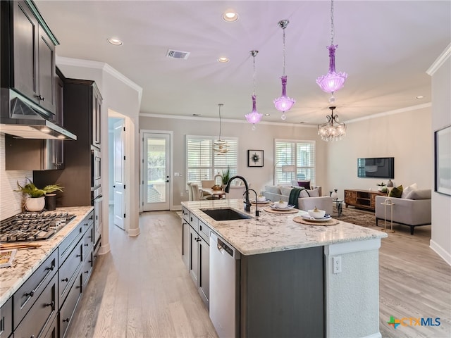 kitchen featuring sink, decorative light fixtures, stainless steel appliances, and a center island with sink