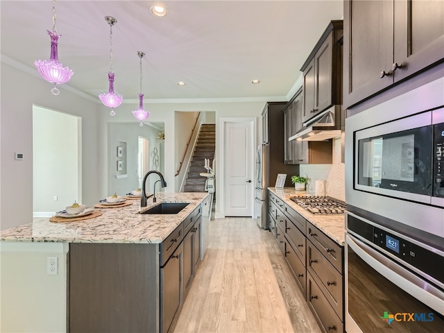 kitchen with light stone counters, stainless steel appliances, a kitchen island with sink, and hanging light fixtures