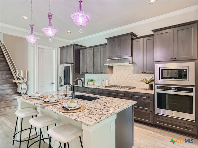 kitchen featuring a kitchen island with sink, decorative light fixtures, light stone countertops, and appliances with stainless steel finishes