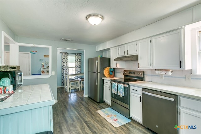 243 E Magnolia Ave, Aransas Pass, TX 78336 - kitchen featuring stainless steel appliances, under cabinet range hood, white cabinets, dark wood-style flooring, and tile countertops