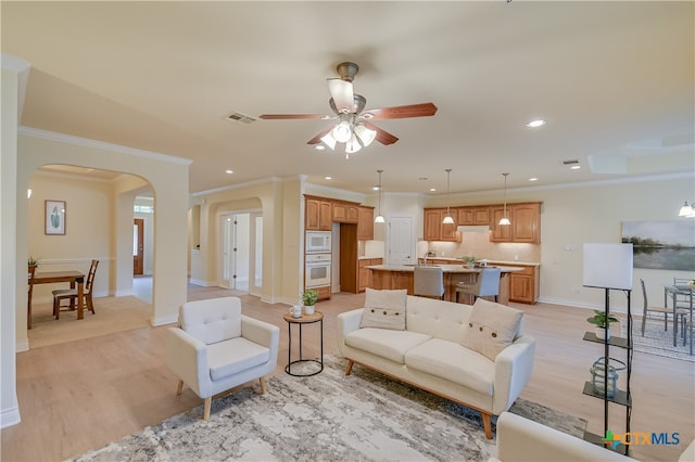 living area featuring ornamental molding, arched walkways, visible vents, and light wood finished floors