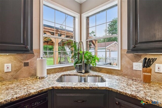 interior details featuring backsplash, dark brown cabinets, a sink, light stone counters, and black dishwasher
