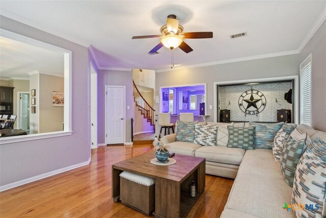 living room with stairs, a ceiling fan, wood finished floors, visible vents, and ornamental molding