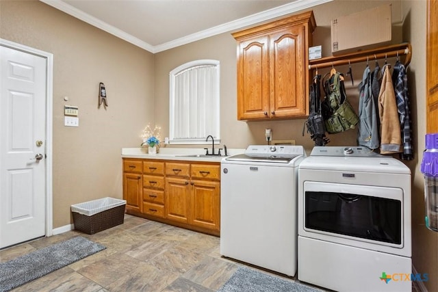 clothes washing area with stone finish flooring, cabinet space, a sink, ornamental molding, and washer and clothes dryer