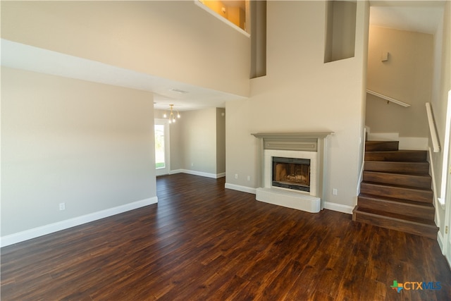 unfurnished living room with dark wood-type flooring, a towering ceiling, and an inviting chandelier