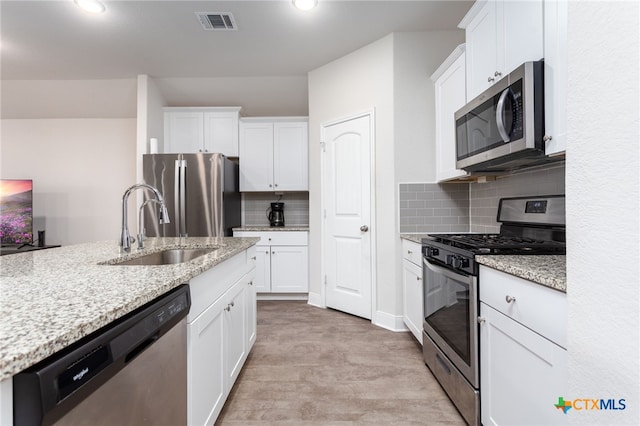 kitchen featuring light stone counters, stainless steel appliances, visible vents, white cabinetry, and a sink