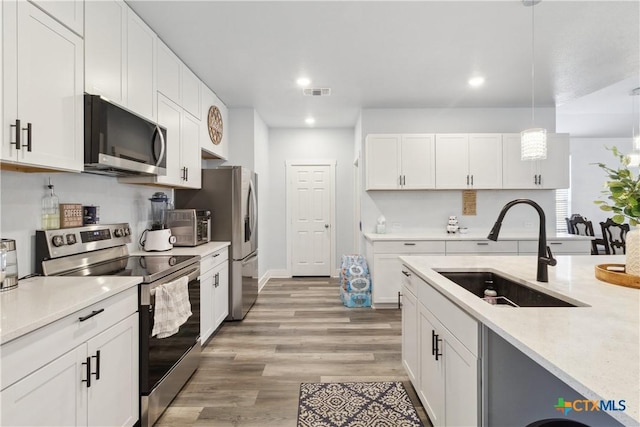 kitchen featuring appliances with stainless steel finishes, decorative light fixtures, sink, white cabinetry, and light hardwood / wood-style floors