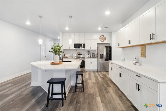 kitchen featuring stainless steel appliances, white cabinetry, hanging light fixtures, and a kitchen island