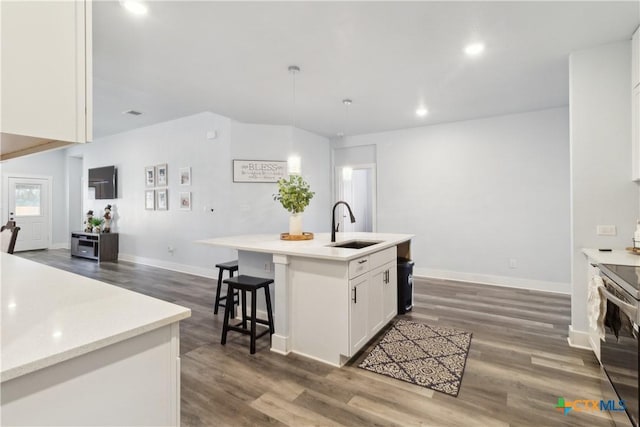 kitchen with white cabinets, stainless steel range with electric stovetop, sink, dark wood-type flooring, and an island with sink