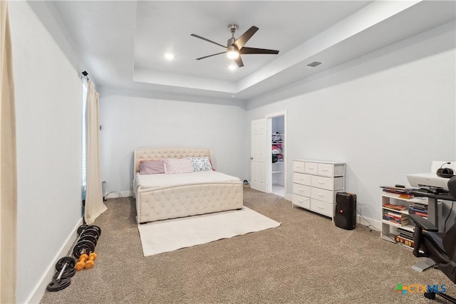 bedroom with a walk in closet, ceiling fan, a raised ceiling, and carpet floors