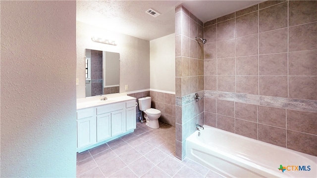 full bathroom with a textured ceiling, vanity, tile patterned floors, toilet, and tiled shower / bath combo