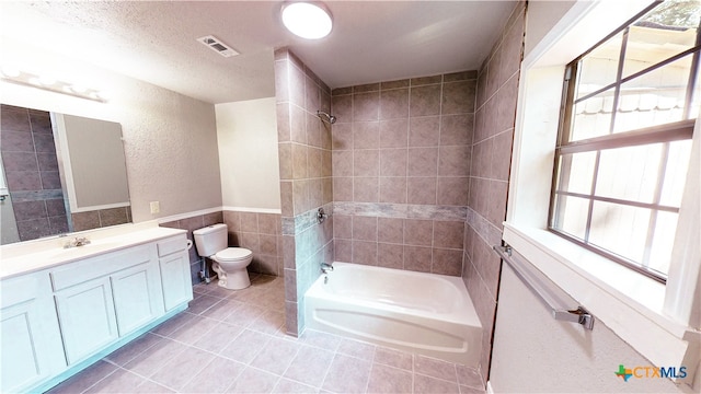 full bathroom featuring toilet, tile walls, tile patterned flooring, tiled shower / bath combo, and vanity