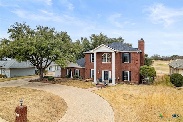 neoclassical home featuring brick siding, a chimney, and curved driveway