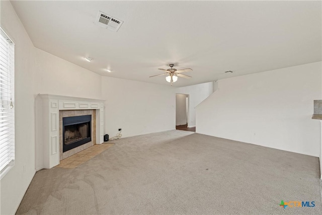 unfurnished living room with a tiled fireplace, light colored carpet, and ceiling fan