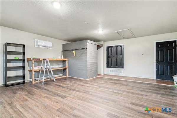 basement featuring wood-type flooring, a wall mounted AC, and a textured ceiling