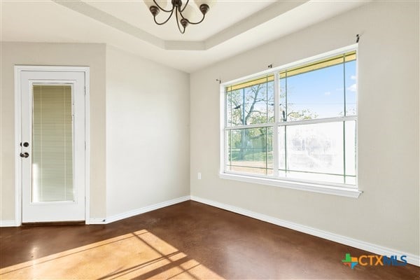 unfurnished room with an inviting chandelier and a raised ceiling