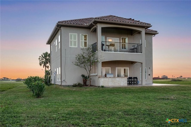 261 E Burgundy Bay Prt, Oconnor, TX 77982 - back of house at dusk with a patio, a yard, stucco siding, and a balcony