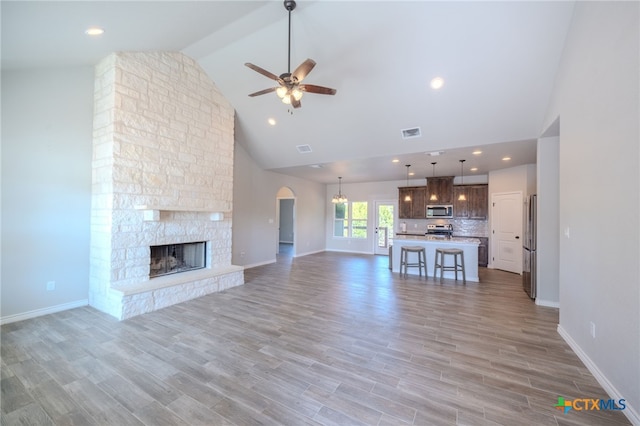 unfurnished living room featuring arched walkways, visible vents, light wood-style floors, a ceiling fan, and a stone fireplace